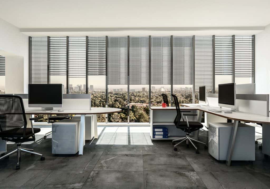 Modern business office with multiple workstations around table style desks with cabinets, tiled grey floor and large windows with blinds. 3d Rendering.